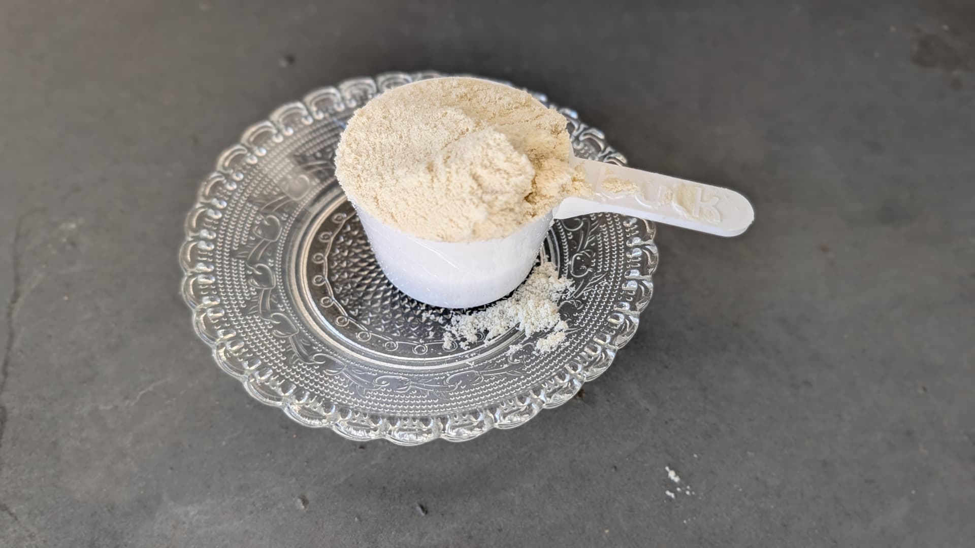 Dosis de creatina en polvo sobre plato de cristal, vista cenital sobre fondo gris
